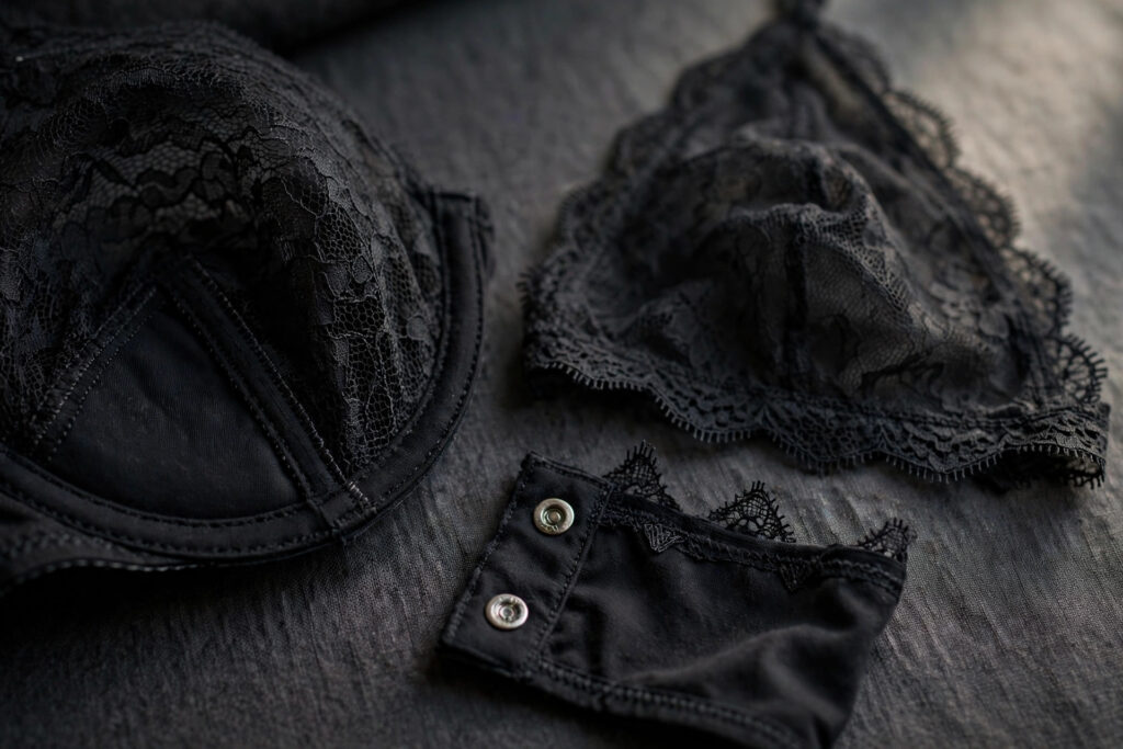 Close-up of black lace lingerie construction details: an underwired lace cup, a soft unstructured lace cup, and a snap-button gusset.
