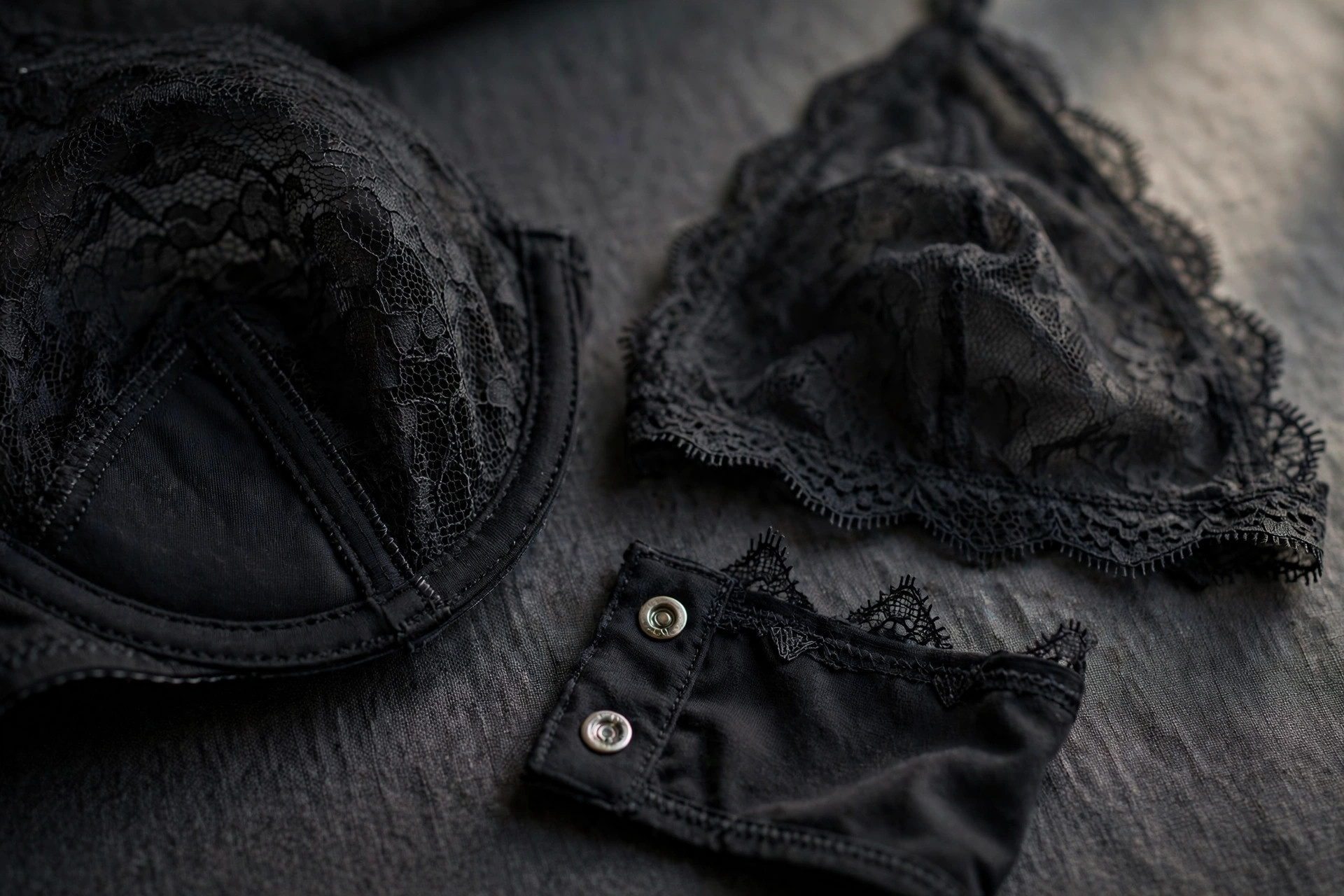 Close-up of black lace lingerie construction details: an underwired lace cup, a soft unstructured lace cup, and a snap-button gusset.
